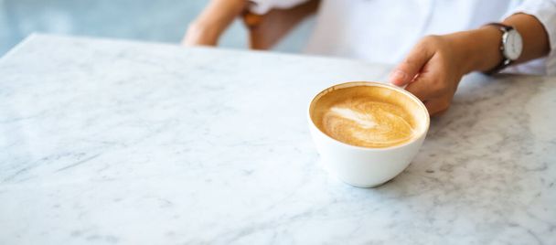 Крупный план женщины, держащей чашку горячего кофе на столе - Фото, изображение