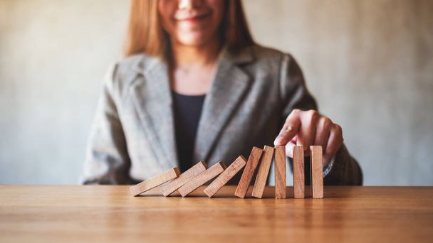 Closeup image of a businesswoman try to use finger to stop falling wooden dominoes blocks for business solution concept  - Foto, imagen