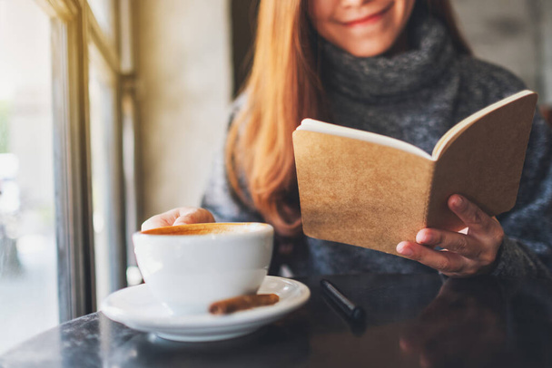 Closeup image of a beautiful woman reading a book while drinking coffee in the morning - Photo, image