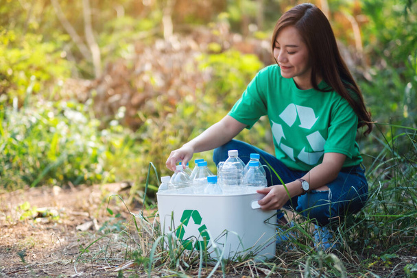 A beautiful asian woman collecting garbage plastic bottles into a recycle bin in the outdoors - Фото, изображение