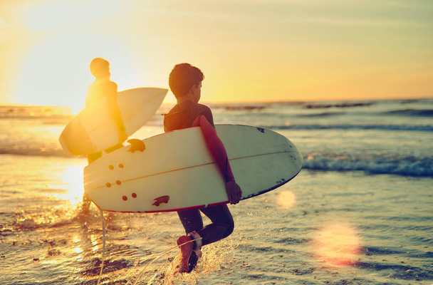 Pysykää rauhallisina ja surffatkaa. Laukaus kahdesta nuoresta veljestä, jotka kantavat surffilautaa kahlatessaan mereen.. - Valokuva, kuva