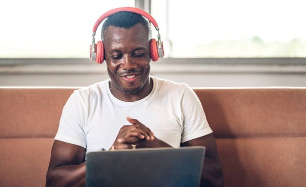 Jeune homme noir africain se détendre à l'aide d'un ordinateur portable travail et vidéo conférence réunion à la maison.Jeune homme africain créatif parler avec headset.work concept de la maison - Photo, image