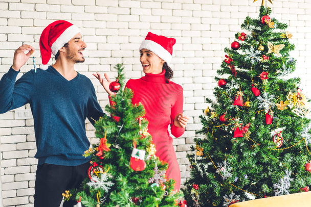 Romantische süße Pärchen in Weihnachtsmützen haben Spaß beim Schmücken des Weihnachtsbaums und lächeln, während sie Silvester feiern und die gemeinsame Zeit in der Weihnachtszeit zu Hause genießen - Foto, Bild