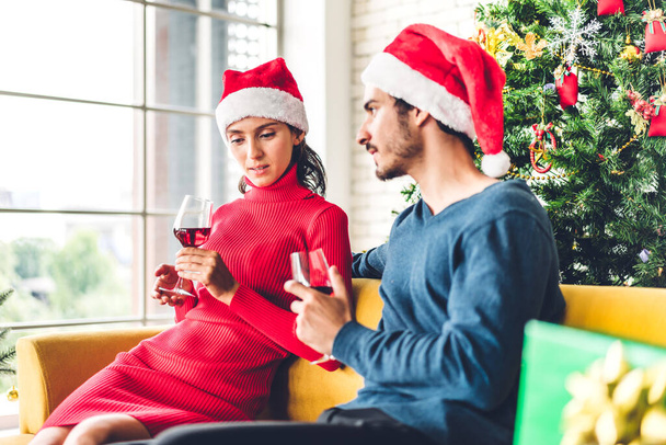 Romantic sweet couple in santa hats having fun and drinking wine glasses while celebrating new year eve and enjoying spending time together in christmas time at home - Фото, изображение