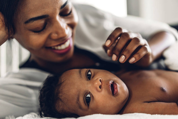 幸せな愛の家族の肖像画アフリカ系アメリカ人の母親は愛らしい小さなアフリカ系アメリカ人の赤ちゃんと遊んでいます.お母さんは白い寝室で楽しい時間をかわいい息子の瞬間に触れて.黒人家族の愛 - 写真・画像