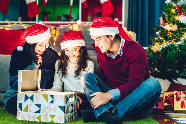 Портрет щасливої сім'ї батька і матері з дочкою в капелюхах Санти весело відкриваючи чарівну різдвяну подарункову коробку і насолоджуючись проведенням часу разом у різдвяний час вдома
 - Фото, зображення