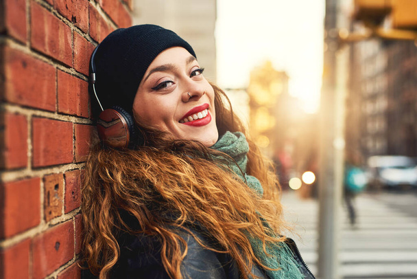 A música é a melhor terapia. Tiro cortado de uma jovem mulher ouvindo música enquanto se inclina contra uma parede de tijolo fora. - Foto, Imagem