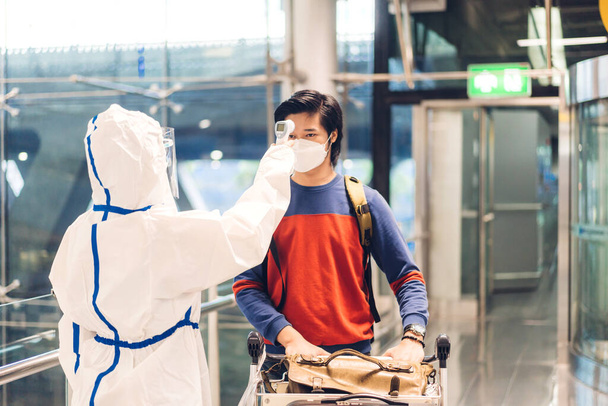 Lekarz kobieta używać podczerwieni termometr czołowy do kontroli temperatury ciała skanowania podróży gorączka pasażera w kwarantannie dla koronawirusu noszenia maski ochronnej na międzynarodowym lotnisku terminalu - Zdjęcie, obraz