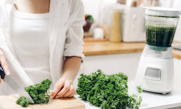 Femme saine profiter de faire des légumes verts désintoxication nettoyer et fruits verts smoothie avec mélangeur dans la cuisine à la maison. - Photo, image