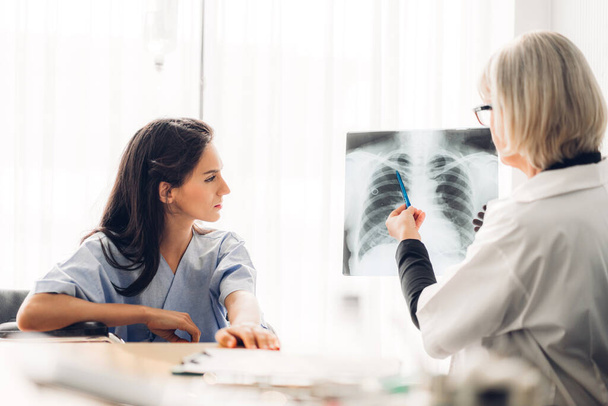 Oberärztin in Uniform mit Stethoskop-Service hilft bei der Diskussion und Betrachtung von Röntgenaufnahmen der Brust einer Patientin mit Lungenentzündung. Gesundheitswesen und Medizin - Foto, Bild