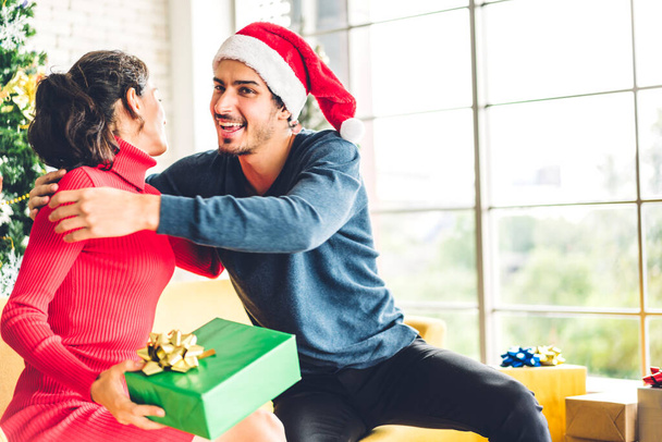 Romantický sladký pár v Santa klobouky baví zdobení vánoční stromeček a usmívat se při oslavě Silvestr a užívat si trávení času. muž dává dárek box překvapení pro ženu - Fotografie, Obrázek