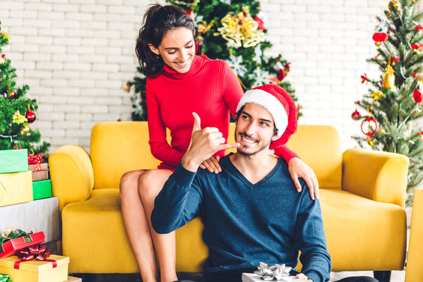 Romantic sweet couple in santa hats having fun decorating christmas tree and smiling while celebrating new year eve and enjoying spending time together.man giving gift box surprise to woman - Foto, afbeelding