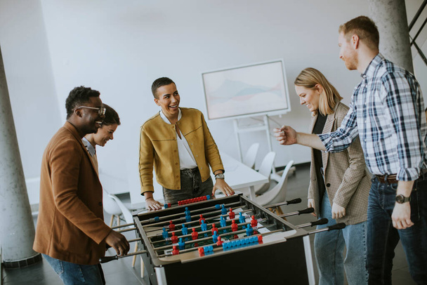 Young handsome casual multiethnic business people playing table football and relaxing at office - Photo, Image