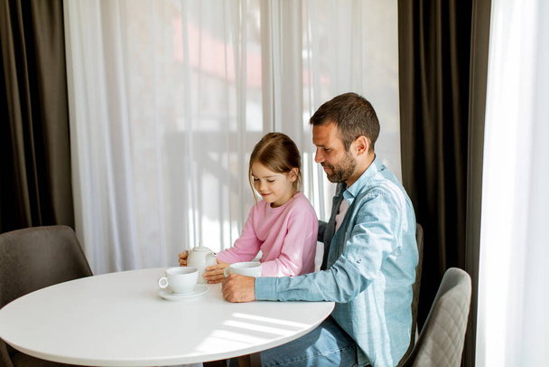 Apa és lánya együtt teáznak a nappaliban. - Fotó, kép