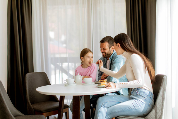 Onnellinen nuori perhe syö kakkuja ja juo teetä yhdessä huoneessa - Valokuva, kuva