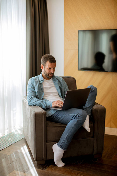 Красивий молодий чоловік використовує ноутбук у вітальні
 - Фото, зображення