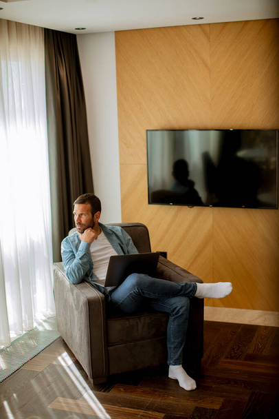 Knappe jongeman met laptop in de woonkamer - Foto, afbeelding