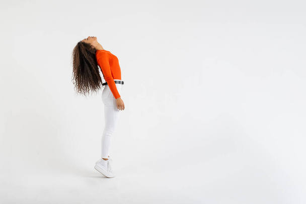 Jeune femme debout sur la pointe des pieds jetant sa tête en arrière sur fond blanc - Photo, image