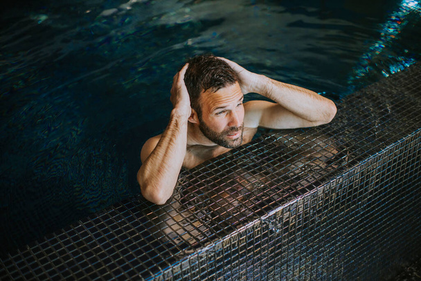 Retrato de joven guapo sonriente relajándose junto al borde de la piscina - Foto, imagen