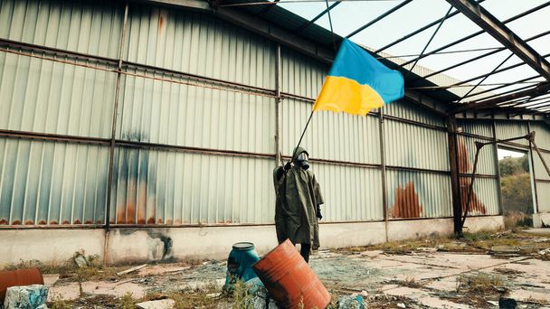 Soldat mit Gasmaske schwenkt ukrainische Flagge in einem Kriegslager - Foto, Bild