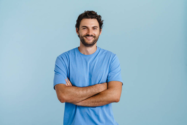 Young brunette man with bristle smiling and looking at camera isolated over blue background - Foto, afbeelding