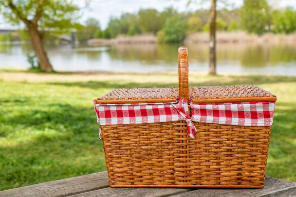 Piknik kosár egy asztalon a ligetben a folyó mellett. Pihenés és nyári hangulat.  - Fotó, kép
