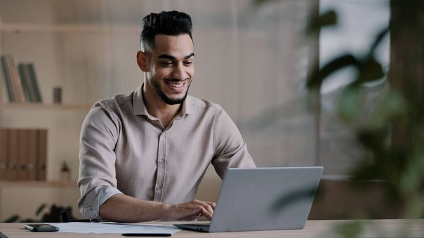 Smiling happy arab man worker businessman finished task computer work relax sit at workplace desk put hands behind head feel satisfied with work well done stress relief taking break after success deal - Foto, Imagen