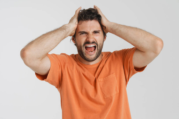 Young brunette man with bristle screaming while holding his head isolated over white background - Photo, Image