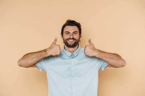 Young white man wearing shirt smiling and showing thumbs up isolated over beige background - Fotografie, Obrázek