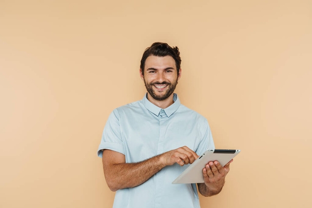 White bristle man smiling and using tablet computer isolated over beige background - Foto, immagini