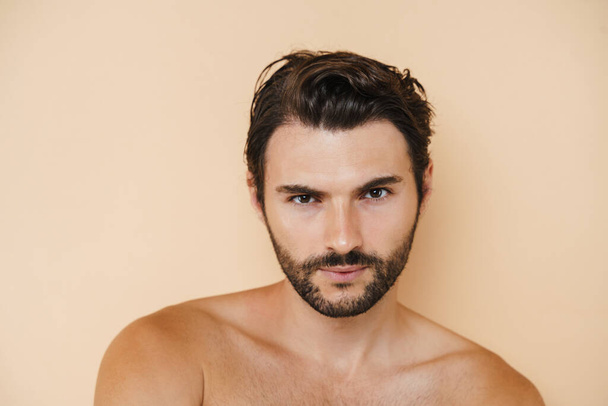 Young half-naked man posing and looking at camera isolated over beige background - Foto, Imagen