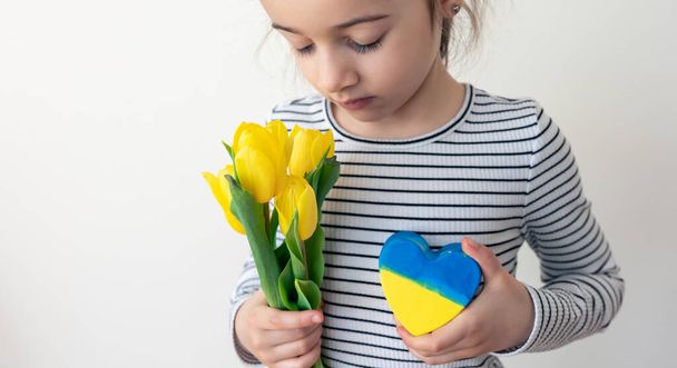 Маленька дівчинка з букетом тюльпанів і серцем з прапором України.. - Фото, зображення