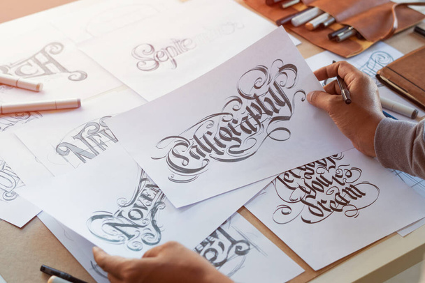 Typografie Kalligrafie kunstenaar ontwerper tekening schets schrijft laten gespeld pen penseel inkt papier tafel artwork.. - Foto, afbeelding