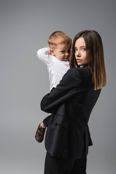 young businesswoman and her little son looking at camera isolated on grey - Photo, Image