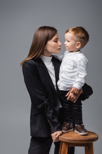 toddler boy standing on high stool face to face with young mom isolated on grey - Photo, Image