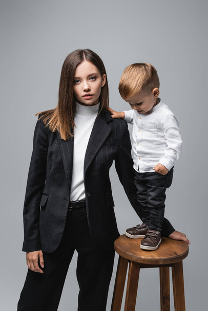 little boy standing on high stool near mother looking at camera isolated on grey - Φωτογραφία, εικόνα