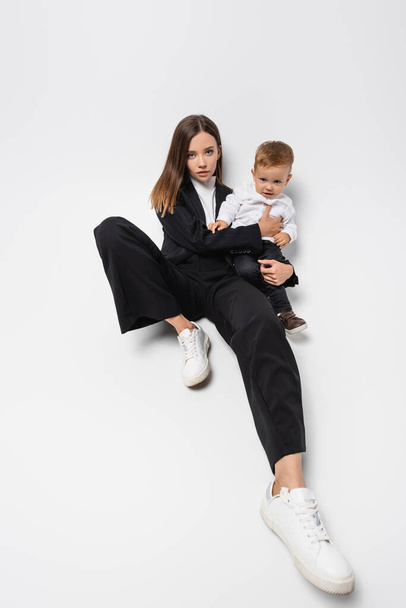 young woman in black suit sitting with little son on white - 写真・画像