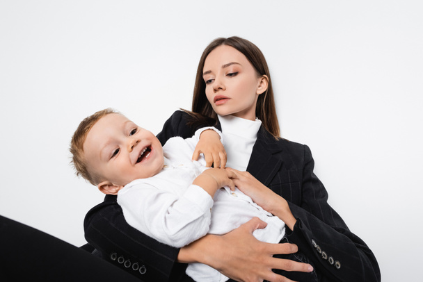 happy boy laughing near mother in black suit isolated on white - Φωτογραφία, εικόνα