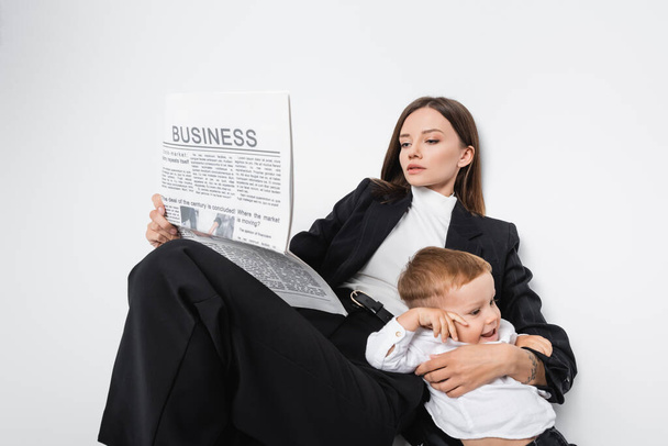 woman in black suit reading business newspaper near happy son on white - Foto, imagen