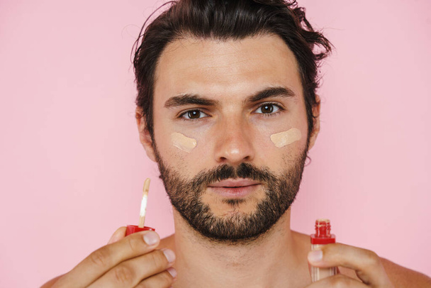 Young half-naked man showing and applying foundation isolated over pink background - Fotoğraf, Görsel