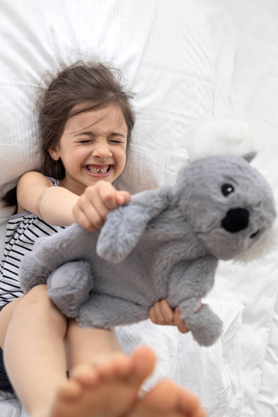 Ευτυχισμένο κοριτσάκι με μαλακό παιχνίδι κοάλα στο κρεβάτι. - Φωτογραφία, εικόνα
