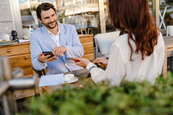 Young man and woman using cellphones during business meeting at cafe outdoors - Φωτογραφία, εικόνα