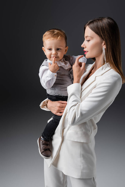 mother and son in stylish clothes touching lips on grey - Fotoğraf, Görsel