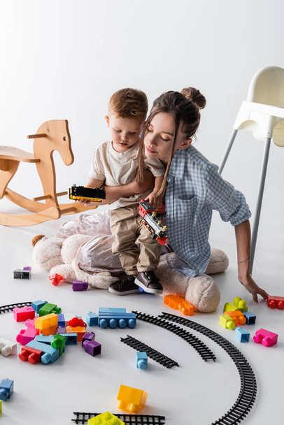 little boy with young mother playing with toy railway on white - Foto, Bild
