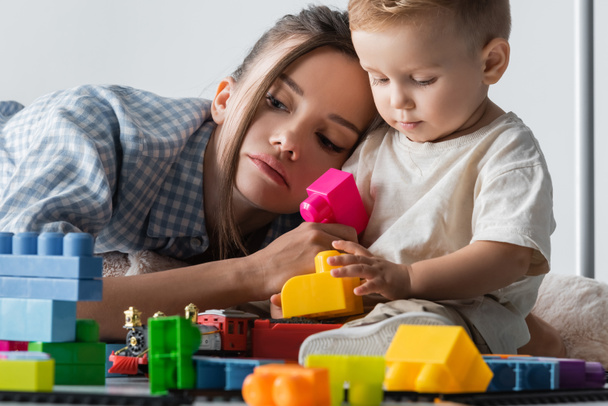 little boy playing with construction cubes near tired mom on grey - Foto, Imagem