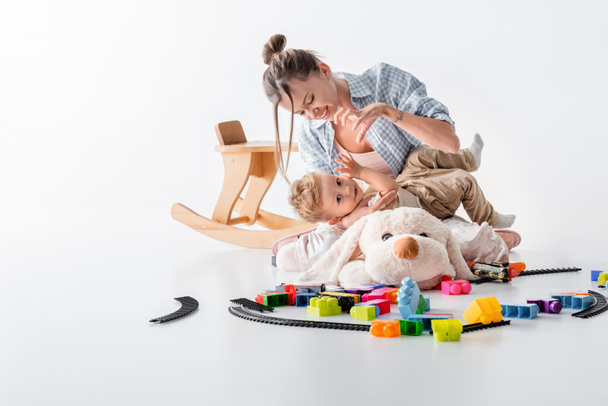 mother showing scary gesture to little son while playing near toys on floor on white - Foto, immagini