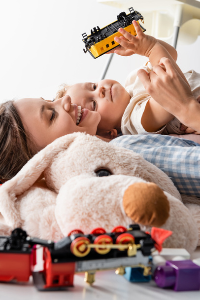 šťastná žena a chlapec s hračkou vlak ležící v blízkosti rozmazané měkké hračky izolované na bílém - Fotografie, Obrázek