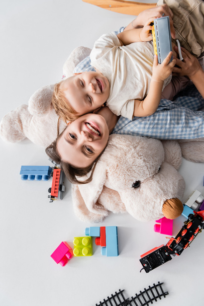 top view of cheerful woman and toddler son lying on huge soft toy on white - Photo, Image