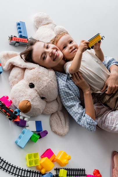 top view of happy woman lying with toddler son on toy dog on grey - Фото, изображение