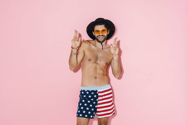 Young shirtless man wearing shorts laughing and gesturing at camera isolated over pink background - Fotó, kép
